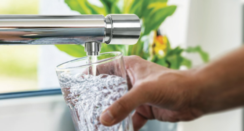 Man holding glass as it's being filled with water flowing from a timed tap